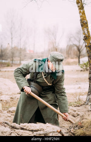 Unidentified Re-enactor Dressed As A German Infantry Soldier Of The World War Ii Digging A Trench In Autumn Forest. Stock Photo