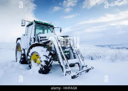 Snow covered green tractor with yellow wheel hubs in North York Moors National Park Stock Photo