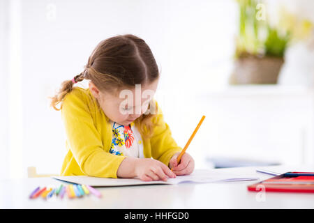 Cute little girl doing homework, reading a book, coloring pages, writing and painting. Children paint. Kids draw. Stock Photo