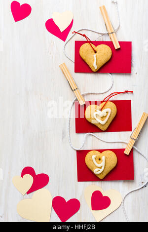 Paper hearts and heart shape cookies hanging on string with mini clothes pin over white wooden board Stock Photo