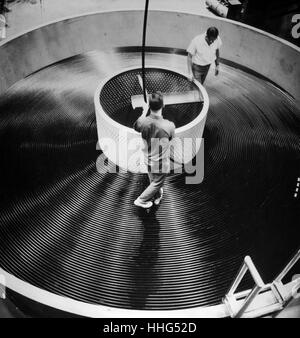 Ocean Cable - Workmen at the Western Eclectic company plant in Baltimore store a 23-mile length of armorless ocean cable in a tank for transfer to the new cable laying ship long lines. The cable will provide a direct telephone link between the United States and Great Britain. Stock Photo