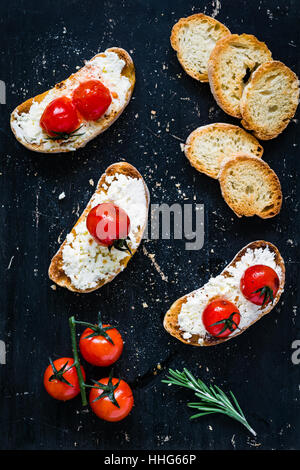 Toast crostini bruschetta with fresh white cheese ricotta, roasted cherry tomatoes and garlic olive oil. Top view Stock Photo