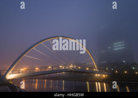 Foggy view of a river, lit bridge and skyscraper in Incheon, South Korea in the evening. Stock Photo