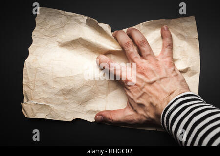 Strong sailor hand catching empty old crumpled paper sheet over black background, pirate map concept Stock Photo