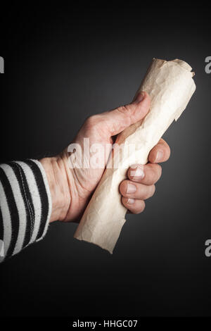 Strong sailor hand holds rolled old crumpled paper sheet over black background, pirate map   concept Stock Photo