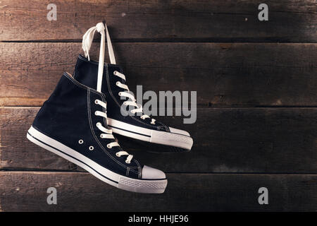 pair of sneakers hang on a nail on a old wooden plank background Stock Photo