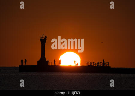 The silhouette of fishermen on Manitowoc, Wisconsin's south pier as the sun peaks over the horizon. Stock Photo