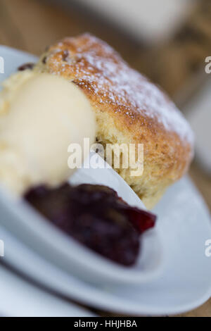 Home made scone dusted with icing sugar, clotted cream and jam on white crockery Stock Photo