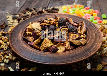 Dried fruit (apples, pears, apricots), berries, raisins and nuts in a bowl on dark wooden background. Close up Stock Photo