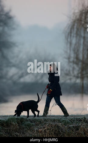 A dog walker along the banks of the banks of the River Great Ouse at Godmanchester on a frosty morning in Cambridgeshire. Stock Photo
