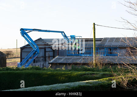 Group of 3 Male workers with hardhats and reflective vests on hydraulic lift in preparation of repair to barn roof, uk Stock Photo