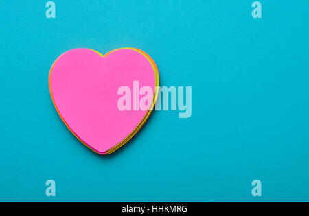 a stack of heart-shaped sticky notes of different colors topped by a pink one with a blank space in it on a blue background with a blank space at the Stock Photo