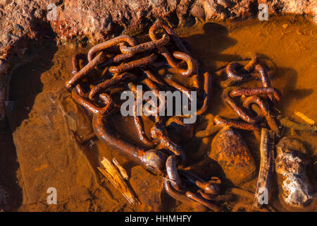 A rusty red chain in a pool of sea water, used to secure boats on the seafront. Stock Photo