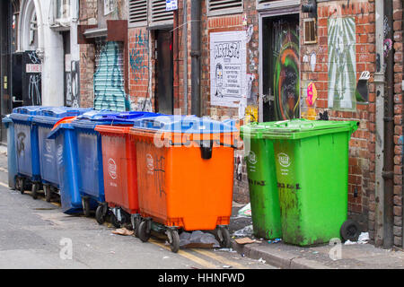 A line of multicoloured dumpsters, Commercial wheelie bins behind stores in Manchester City centre Stock Photo