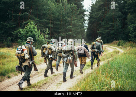 Group Of Unidentified Re-enactors Dressed As German Soldiers Marching Along Forest Road. Summer Season. Stock Photo