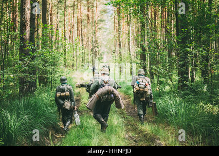 Group Of Unidentified Re-enactors Dressed As German Soldiers Marching Along Forest Road. Summer Season. Stock Photo