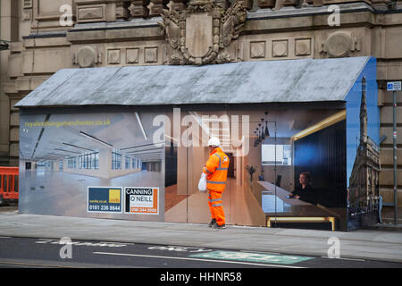 Workman in hi-vis clothing walking past an interior office scene painted on Innovative Hoarding, A unusual building entrance to a construction site in Royal Exchange Building, Market Street,  Manchester, UK. Stock Photo