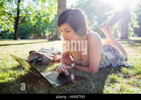 Chinese woman laying on grass using laptop Stock Photo