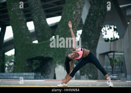 Mixed Race woman stretching under bridge Stock Photo