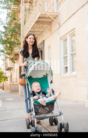 Mother pushing baby son in stroller in city Stock Photo