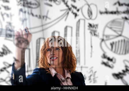 Caucasian businesswoman drawing charts on glass wall Stock Photo