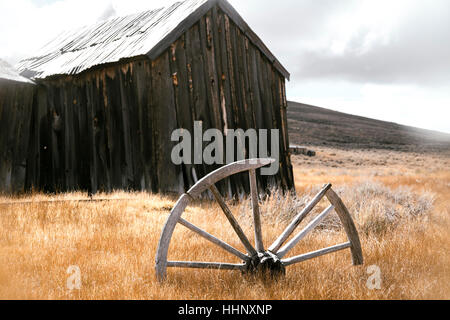 Broken wooden wheel in grass near rustic building Stock Photo