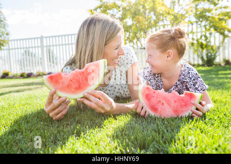 Caucasian mother and daughter laying in grass eating watermelon Stock Photo