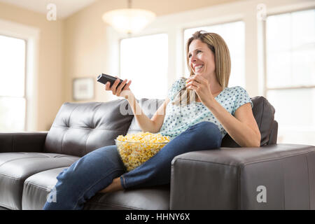 Caucasian woman watching television and eating bowl of popcorn Stock Photo