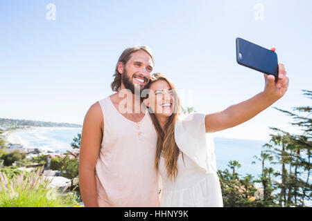 Caucasian couple posing for cell phone selfie at beach Stock Photo