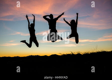 Silhouette of friends jumping for joy at sunset Stock Photo