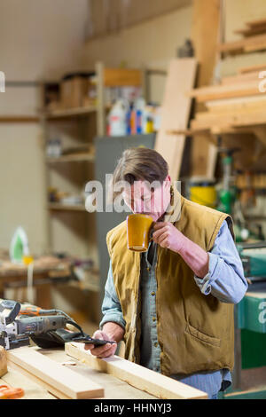 Caucasian carpenter drinking coffee and texting on cell phone in workshop Stock Photo