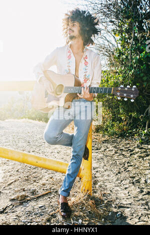 Mixed Race man leaning on gate playing guitar Stock Photo