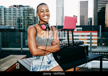 Smiling Black DJ relaxing on urban rooftop Stock Photo