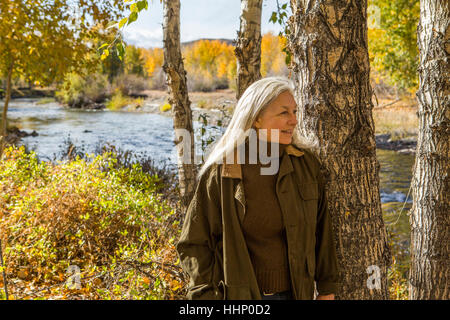 Smiling Caucasian woman leaning on tree near river Stock Photo