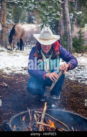 Caucasian woman putting wood in campfire Stock Photo