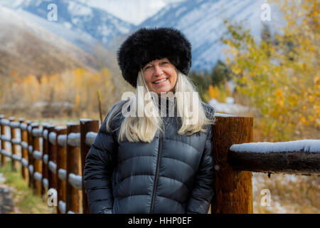 Caucasian woman wearing fur hat leaning on wooden fence in winter Stock Photo