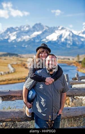 Smiling Caucasian couple posing at wooden fence near river Stock Photo