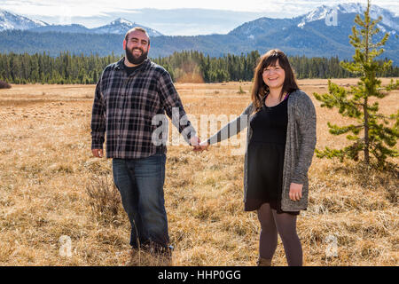 Smiling Caucasian couple holding hands in field Stock Photo