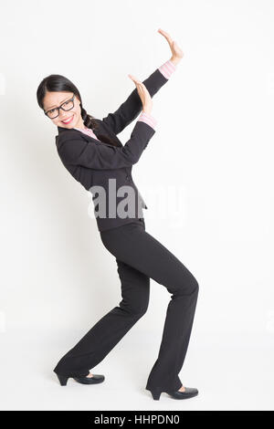 Full body portrait of young Asian businesswoman in formalwear hands defending on something, standing on plain background. Stock Photo