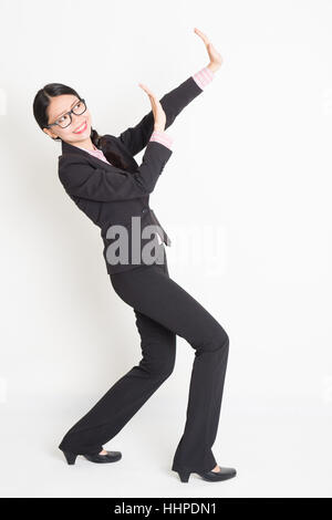 Full body portrait of young Asian businesswoman in formalwear hands defending on something, standing on plain background. Stock Photo