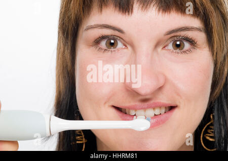 Frontal close-up of a young woman with electric toothbrush on the teeth friendly smiling into the camera. Stock Photo