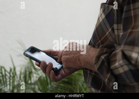 Man's hand holding cell phone in right hand standing outside over greens plants with negative space in upper left  background pointing to home button Stock Photo