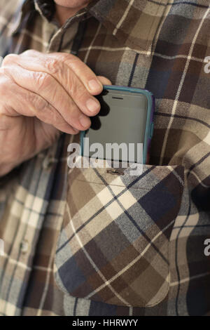 Man's hand with four fingers close together inserting mobile device into left front shirt pocket closeup in vertical format Stock Photo