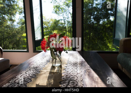 ixora flower in vase on wood table near window with garden view in living room Stock Photo