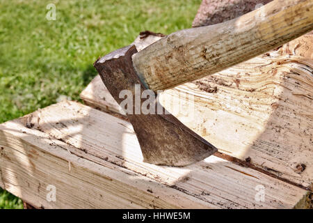 Old rusty ax stuck in a piece of wood in bright sunny day Stock Photo