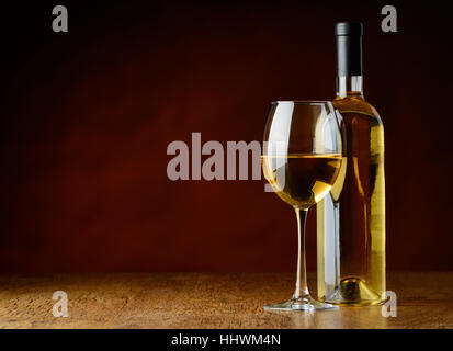 A glass of white wine and a bootle of white wine oni a wooden table in a a winecellar Stock Photo