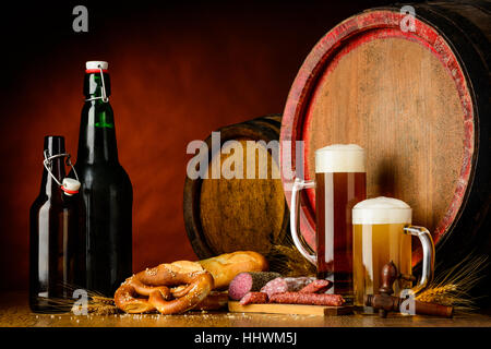 Still life with Beer bottles and glasses in a rustic setup with prezel, sausages, wheat and barrels. Stock Photo