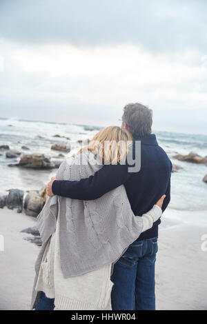 Serene affectionate couple hugging on winter beach looking at ocean Stock Photo