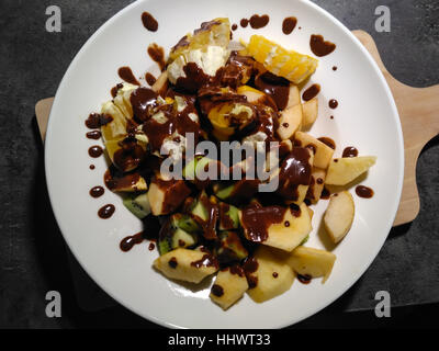 Tasteful apples, oranges, kiwi topped with chocolate on the white plate. Healthy. Stock Photo