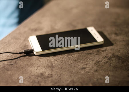 Charging white smart phone on graphite desk. Stock Photo